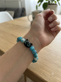 Bracelet perles turquoise avec pendentif tête de chat noir aux yeux turquoise porté sur un poignet