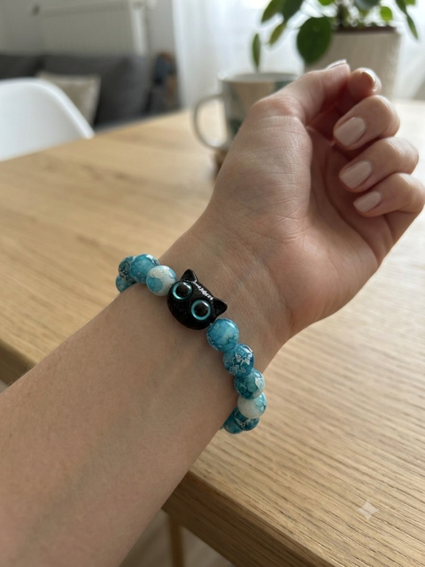 Bracelet perles turquoise avec pendentif tête de chat noir aux yeux turquoise porté sur un poignet