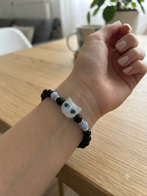 Bracelet perles noires avec pendentif tête de chat blanc aux yeux bleus porté sur un poignet