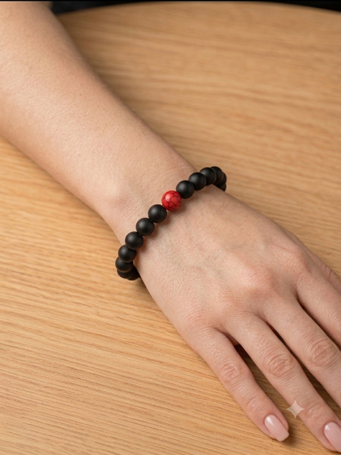 Bracelet perles noires mates avec perle rouge centrale porté sur un poignet